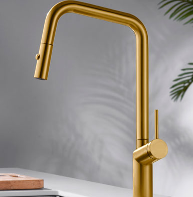 Llave de cocina elegante color dorada tipo oro, con mango extraible de fondo pared blanca con reflejo de hojas verdes